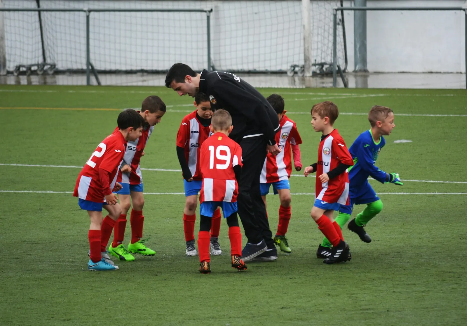 Professor de Educação Física orienta uma turma de alunos reunida em roda no campo, antes do treino