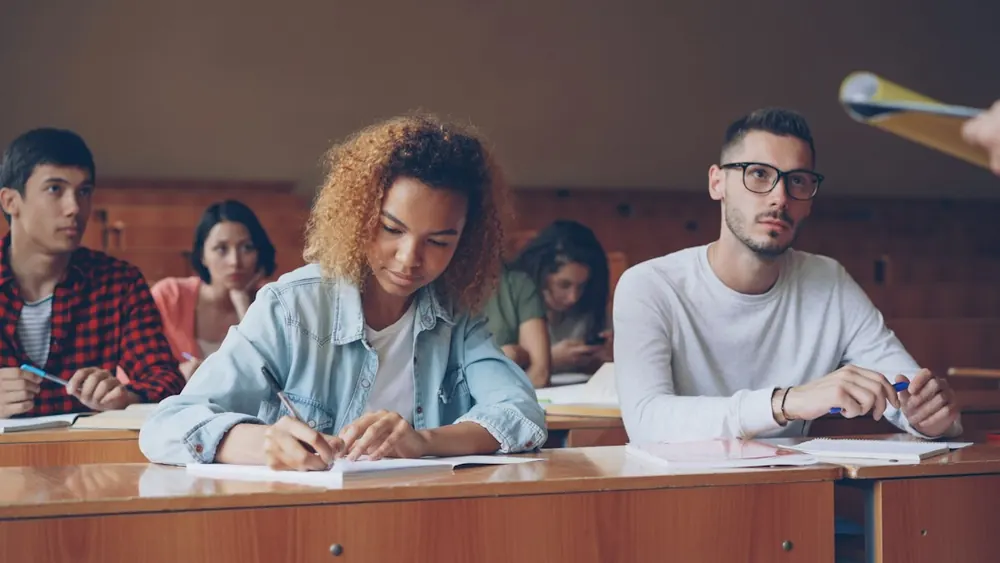 Estudantes atentos em sala de aula, escrevendo durante a aula